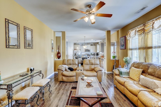 living area with visible vents, wood finished floors, baseboards, and ceiling fan