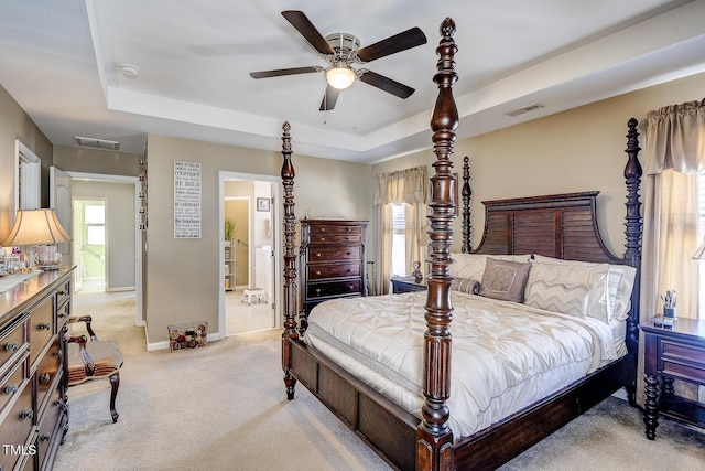 bedroom with a tray ceiling, visible vents, and light carpet