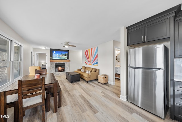 interior space featuring light wood-style flooring, ceiling fan, a lit fireplace, and baseboards