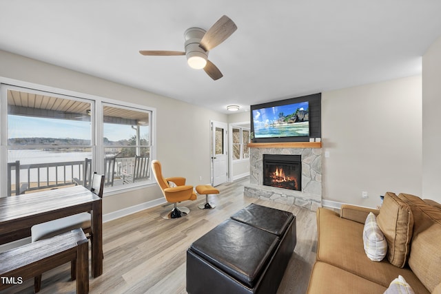 living room featuring a stone fireplace, wood finished floors, a ceiling fan, and baseboards