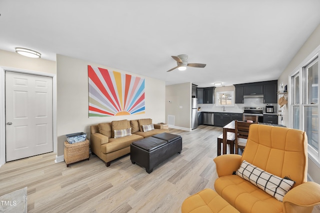 living area featuring light wood-type flooring, ceiling fan, visible vents, and baseboards