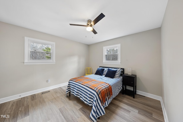 bedroom with a ceiling fan, visible vents, baseboards, and wood finished floors