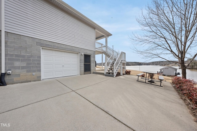 view of side of home with a porch, a water view, a garage, driveway, and stairs