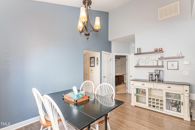 dining area featuring a towering ceiling, visible vents, a chandelier, and wood finished floors