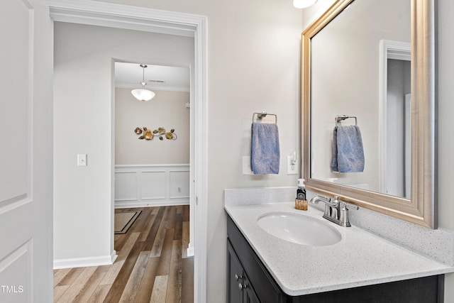 bathroom featuring a decorative wall, ornamental molding, wainscoting, vanity, and wood finished floors