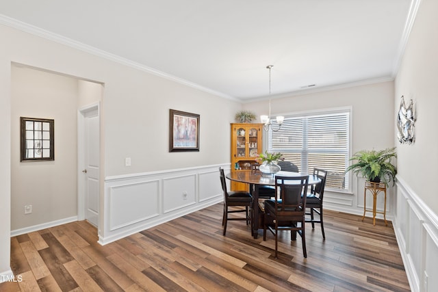 dining room featuring a decorative wall, a wainscoted wall, wood finished floors, visible vents, and crown molding