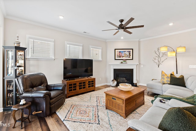 living room with crown molding, visible vents, wood finished floors, and a glass covered fireplace