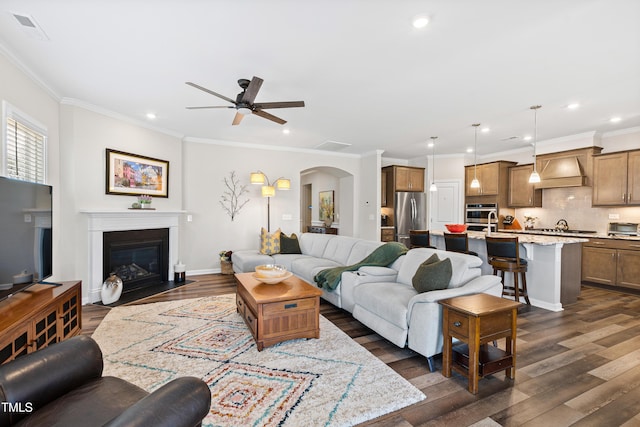 living room featuring arched walkways, ornamental molding, and dark wood finished floors