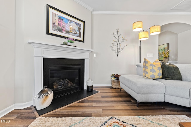 living room featuring baseboards, arched walkways, a glass covered fireplace, wood finished floors, and crown molding