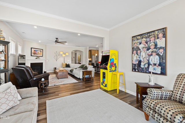 living room featuring baseboards, arched walkways, ornamental molding, wood finished floors, and a fireplace