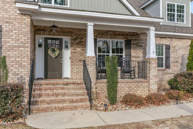 view of exterior entry with covered porch, brick siding, and roof with shingles