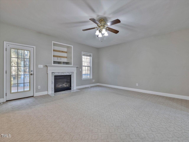 unfurnished living room with a high end fireplace, ceiling fan, baseboards, and carpet