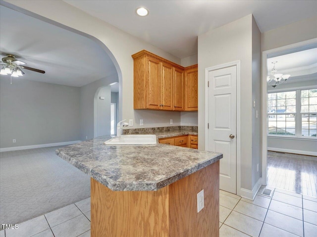 kitchen with light tile patterned floors, a sink, light carpet, ceiling fan with notable chandelier, and brown cabinets