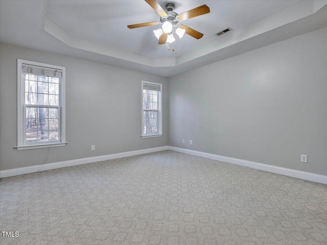 carpeted spare room featuring a tray ceiling, baseboards, visible vents, and a ceiling fan