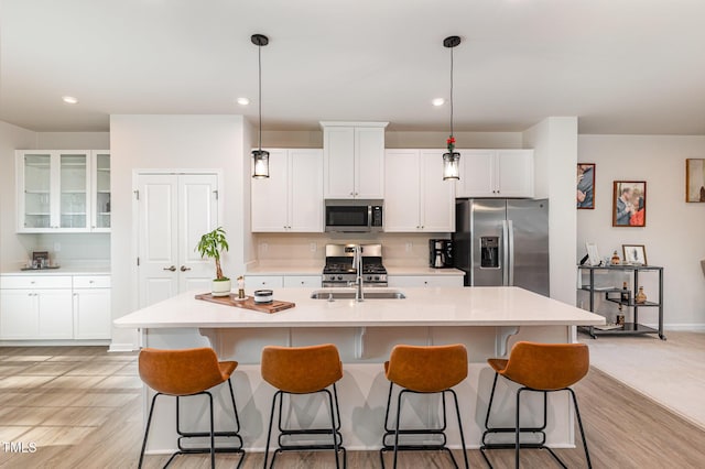 kitchen with a breakfast bar, a center island with sink, white cabinets, and stainless steel appliances