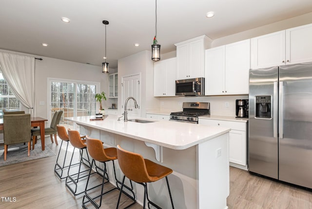 kitchen with light wood-type flooring, a center island with sink, stainless steel appliances, and a sink