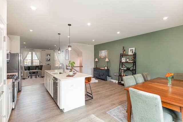 kitchen with a kitchen island with sink, a sink, white cabinetry, appliances with stainless steel finishes, and a kitchen bar