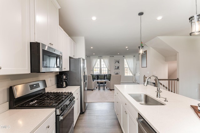 kitchen featuring stainless steel appliances, hanging light fixtures, white cabinetry, a sink, and light wood-type flooring