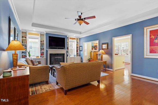 living room featuring a wealth of natural light, a glass covered fireplace, crown molding, and hardwood / wood-style flooring