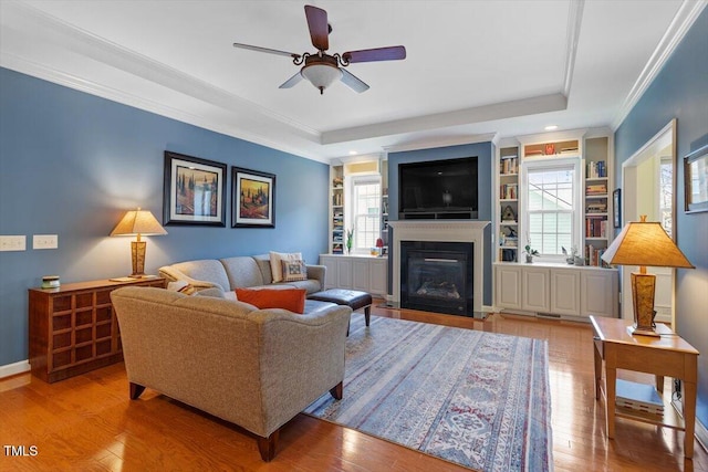 living area with wood-type flooring, a tray ceiling, and ornamental molding