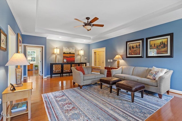 living area with ornamental molding, a raised ceiling, baseboards, and wood finished floors