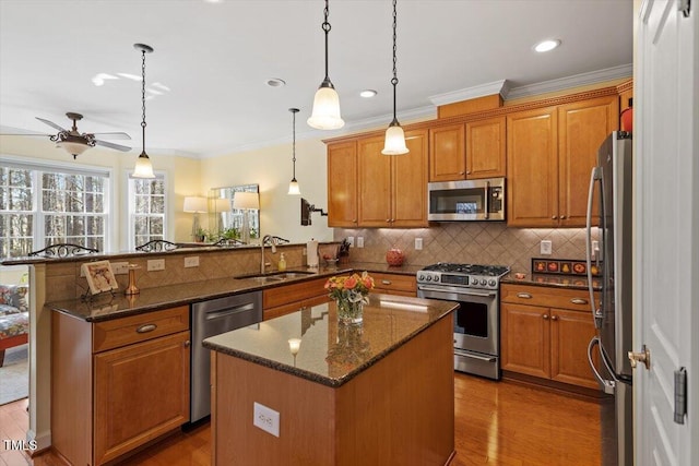 kitchen featuring stainless steel appliances, brown cabinetry, ornamental molding, a sink, and a peninsula