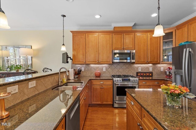 kitchen with brown cabinetry, stainless steel appliances, a sink, and decorative light fixtures