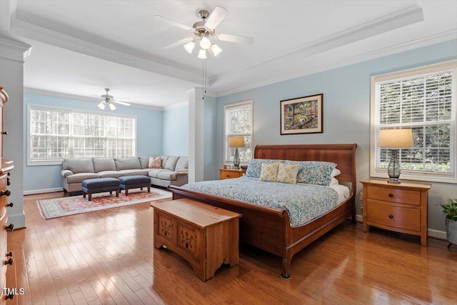 bedroom featuring baseboards, wood-type flooring, a raised ceiling, and crown molding