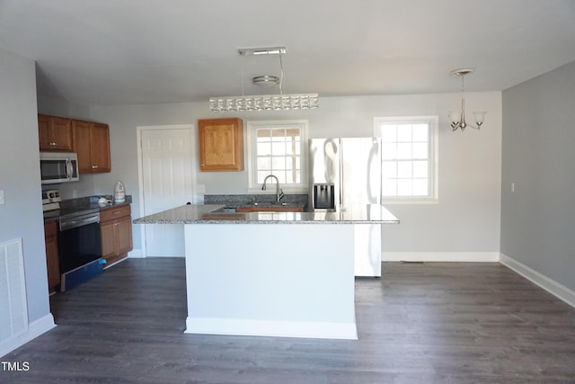 kitchen featuring dark wood-type flooring, a kitchen island, baseboards, appliances with stainless steel finishes, and brown cabinets