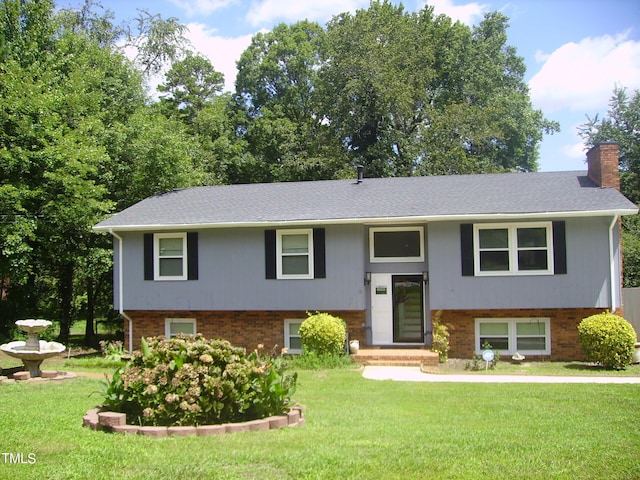 raised ranch featuring brick siding, a chimney, and a front lawn