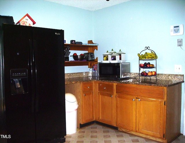 kitchen featuring dark stone countertops, brown cabinets, and black fridge