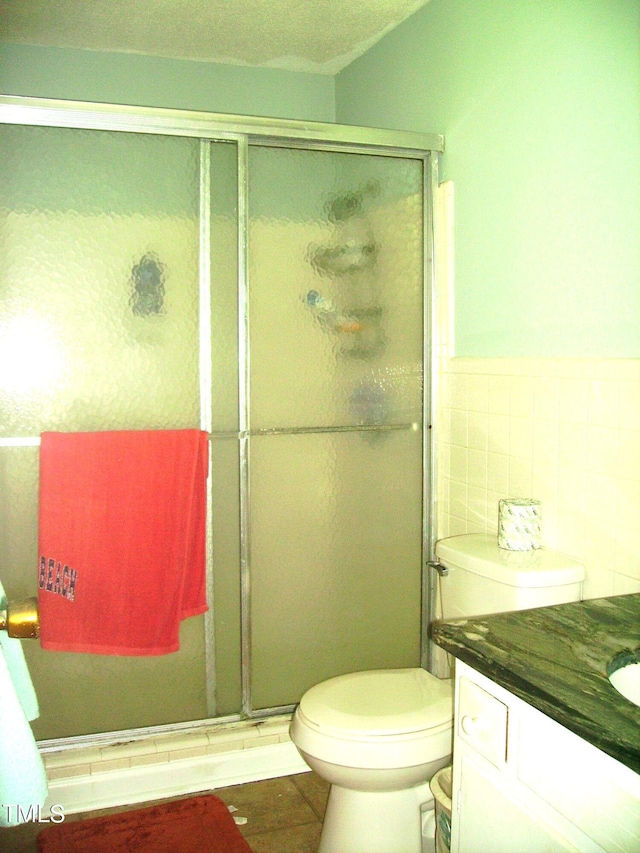 bathroom featuring tile walls, toilet, a stall shower, vanity, and tile patterned flooring