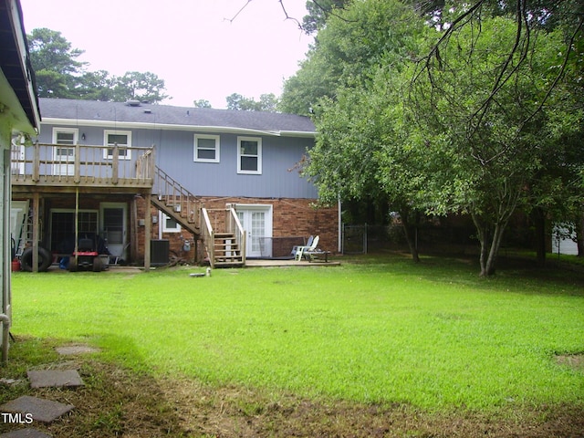 back of house featuring stairs, a deck, a lawn, and brick siding