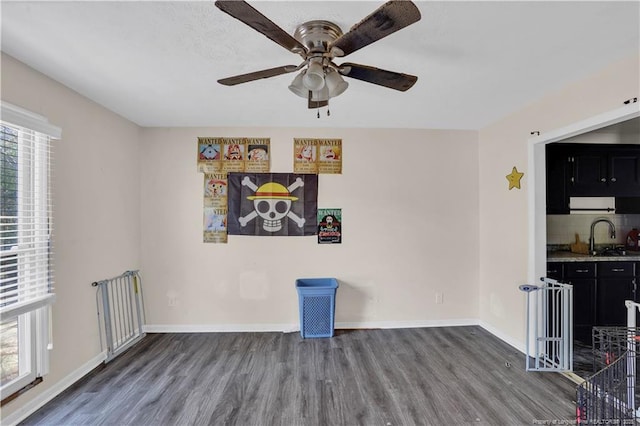 unfurnished dining area featuring a ceiling fan, a sink, baseboards, and wood finished floors