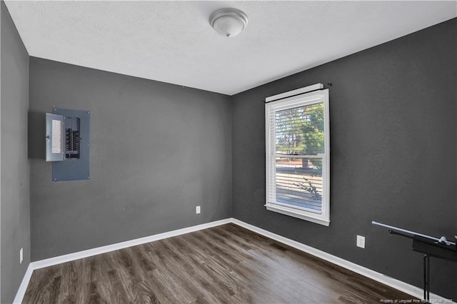 spare room featuring visible vents, wood finished floors, electric panel, and baseboards