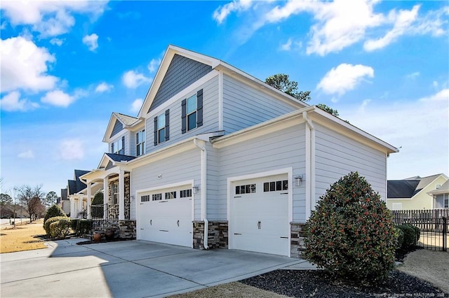 view of home's exterior with a garage, stone siding, driveway, and fence