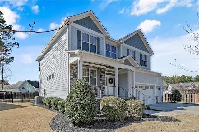 view of front of home featuring central air condition unit, covered porch, fence, concrete driveway, and stone siding