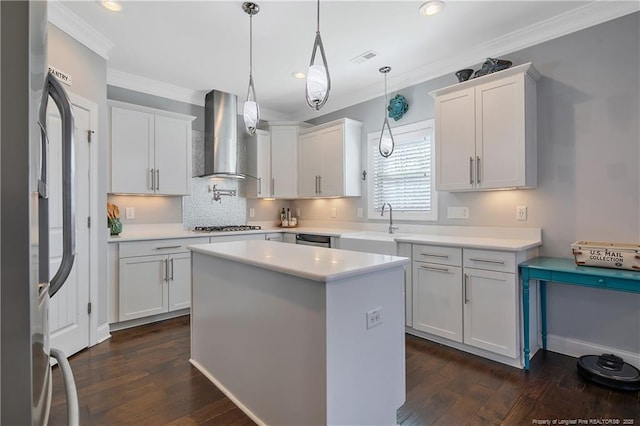 kitchen with dark wood-style floors, wall chimney exhaust hood, ornamental molding, stainless steel appliances, and light countertops