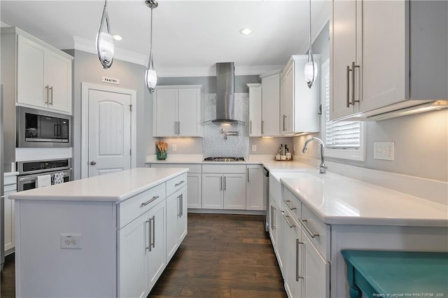 kitchen with white cabinets, a center island, stainless steel appliances, crown molding, and wall chimney range hood