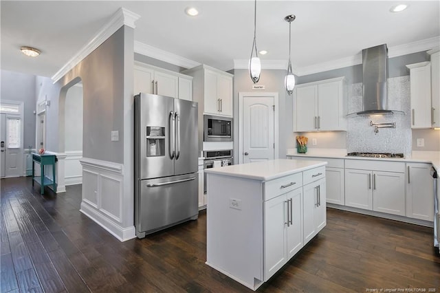 kitchen with white cabinets, a kitchen island, appliances with stainless steel finishes, light countertops, and wall chimney range hood