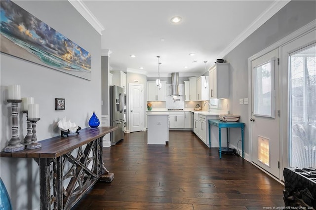 kitchen with stainless steel fridge, ornamental molding, a center island, wall chimney range hood, and a sink