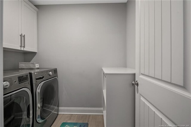 laundry area with cabinet space, baseboards, washer and clothes dryer, and light wood finished floors