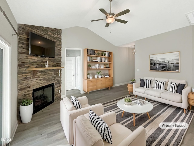 living area with lofted ceiling, a ceiling fan, a stone fireplace, wood finished floors, and baseboards