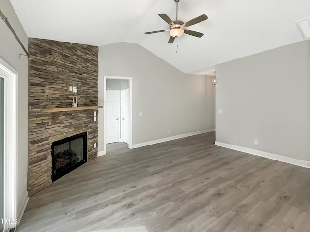 unfurnished living room featuring lofted ceiling, ceiling fan, a stone fireplace, wood finished floors, and baseboards