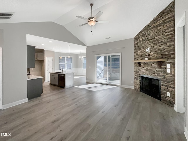 unfurnished living room with ceiling fan, a stone fireplace, light wood-type flooring, and visible vents