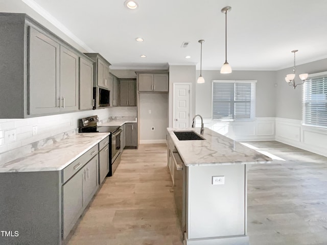 kitchen with wainscoting, appliances with stainless steel finishes, gray cabinetry, light wood-type flooring, and a sink