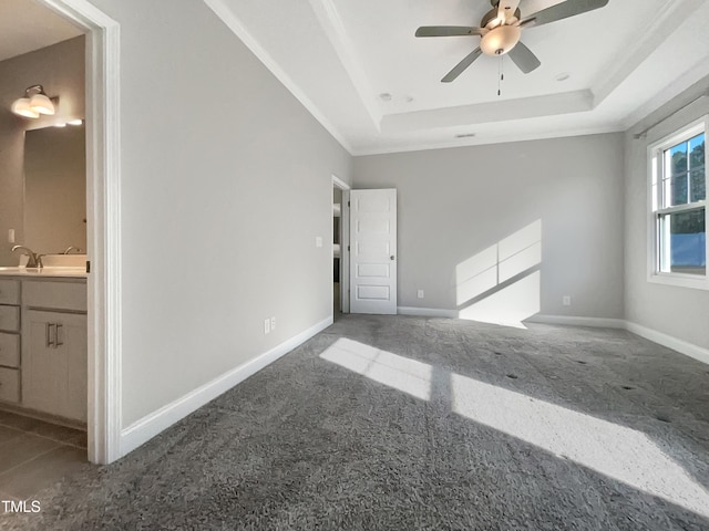 carpeted empty room featuring a tray ceiling, a sink, ceiling fan, and baseboards