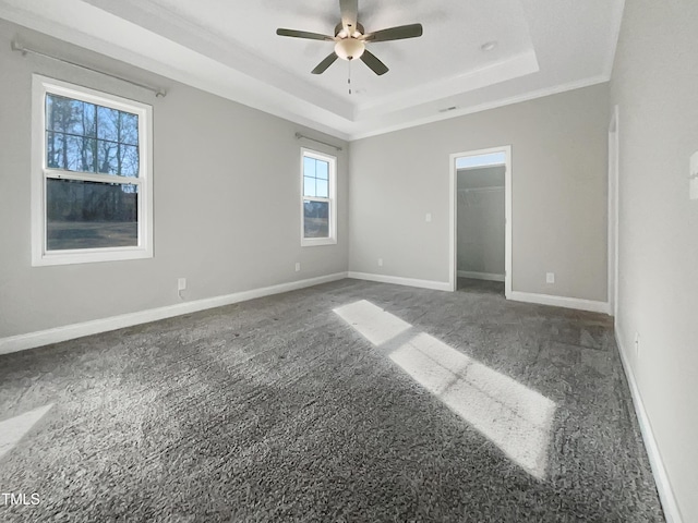 unfurnished bedroom with carpet, baseboards, a tray ceiling, and a walk in closet