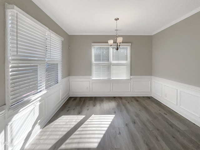 unfurnished dining area featuring a wainscoted wall, a notable chandelier, a decorative wall, ornamental molding, and wood finished floors