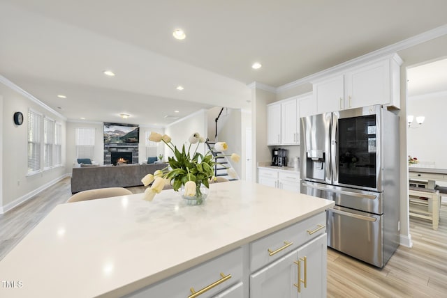 kitchen featuring ornamental molding, white cabinetry, stainless steel fridge, a fireplace, and light wood finished floors